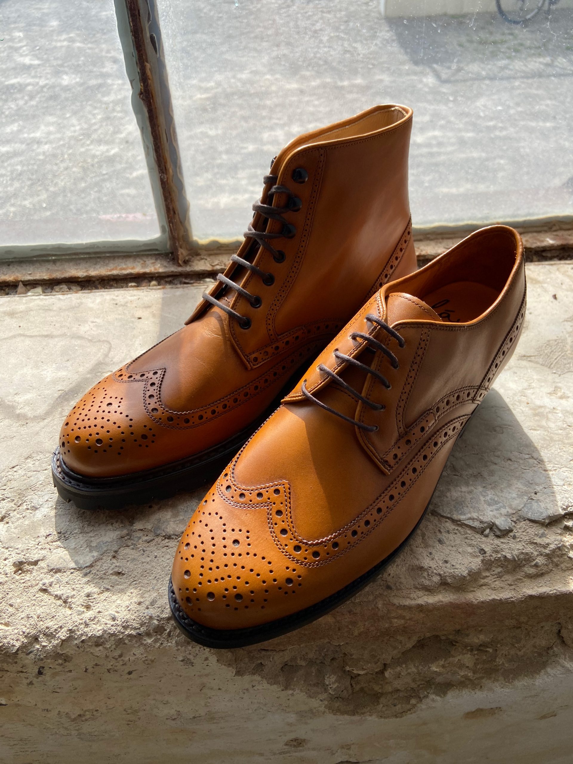 Tan leather brogues, welted construction, on a stone sill.